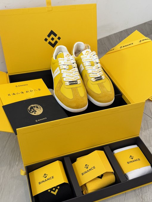 An open yellow Binance-branded box containing yellow sneakers, apparel, and accessories.