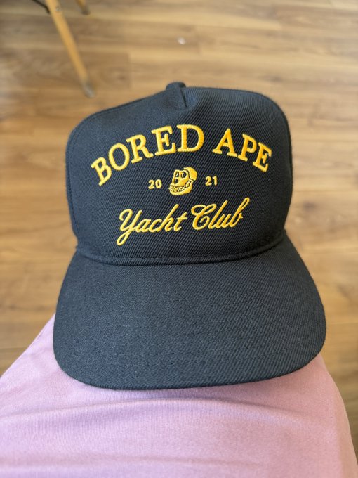 A black snapback hat with yellow embroidered text reading 'BORED APE YACHT CLUB 2021' featuring the iconic ape skull logo.