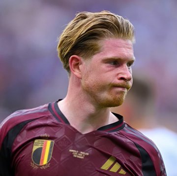 Kevin De Bruyne, wearing Belgium's maroon and yellow kit with the national team crest visible, is shown on the pitch during halftime of the match that ended the first half tied at 1-1.