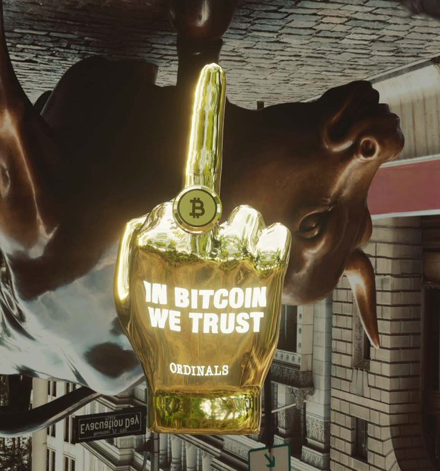 An upside-down golden hand making a rude gesture with a Bitcoin coin on its middle finger, displaying 'IN BITCOIN WE TRUST' and 'ORDINALS' on the palm, set against a brick building and dark sculptural background.