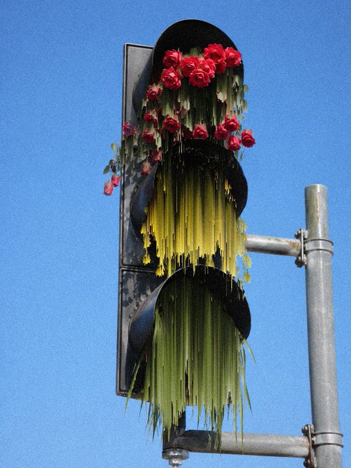 A traffic signal is dramatically draped with red roses and long strands of green, black, and yellow wax-like material against a blue sky. The post title, “Oh, Don’t Stop,” appears to playfully reference the altered stoplight artwork linked via objkt.com.