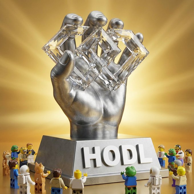 The image features a silver hand sculpture with the word "HODL" written on it, surrounded by Lego minifigures. The group of people are gathered around the sculpture, possibly discussing or admiring its design.