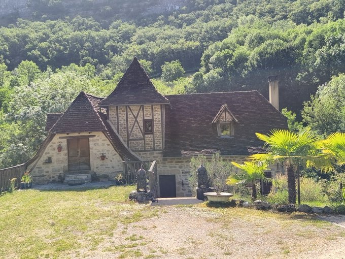 There is a property for sale that has several features, including a stone building with a brown roof, an old-fashioned design that resembles a castle or fortification. The house also has some trees around it, indicating it may be located in the countryside. An interesting detail about this property is that there are two people standing in front of it and another person taking pictures of the house next to a tree.