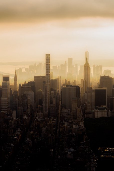 A hazy, golden-hour cityscape view of Midtown Manhattan, featuring the Empire State Building silhouetted against the warm sky.