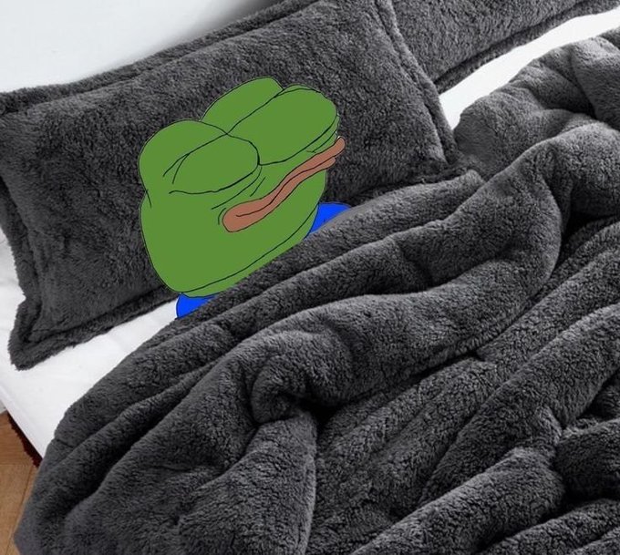 A green cartoon character lies face-down in a bed under a plush gray blanket, with their brown tongue sticking out, resting on a pillow.