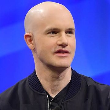 A close-up portrait of a bald man in a black jacket against a blue background.