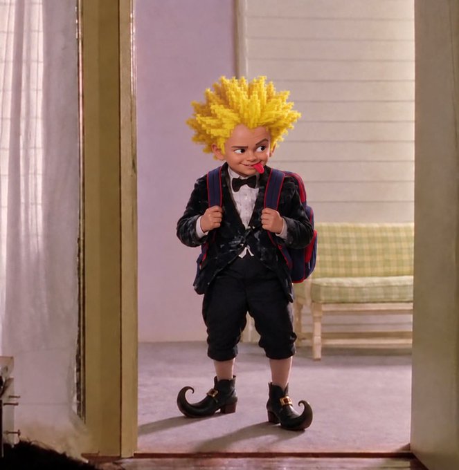A person in costume, styled after the character Davie from the film "Stuart Little," stands in a doorway wearing a yellow spiky wig, a black suit, curled shoes, and a backpack.