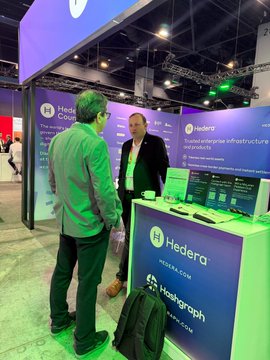 Two men converse at the Hashgraph booth (DISM03) at Sibos, standing in front of a Hedera-branded display highlighting the company's trusted enterprise infrastructure and its three offerings: HashSphere, Asseto, and the CLPR cross-ledger protocol.