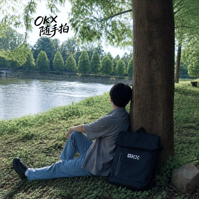 The image features a man sitting under a tree, leaning against it with his back to the viewer. He has a backpack next to him, suggesting that he might be taking a break from traveling or an outdoor adventure. The background of the photo shows a body of water and trees, creating a serene atmosphere for the scene. The image also contains text in Chinese, which could potentially be related to the post's content or context.