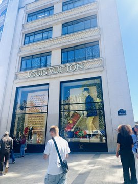 An exterior shot of a Louis Vuitton store with its signature window displays, with people walking by on the street below.