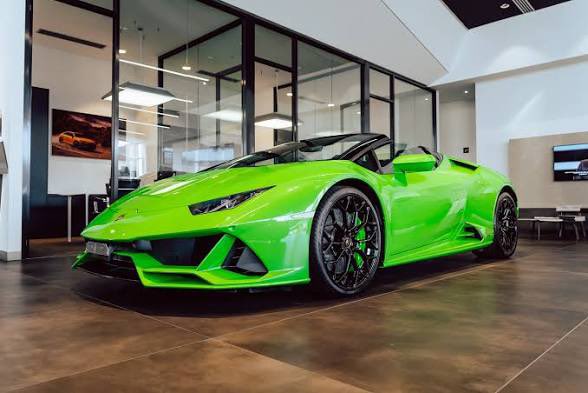 A bright green Lamborghini Huracán EVO Spyder displayed in a modern car showroom with large glass windows and polished floors.