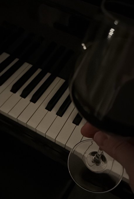 Close-up of a hand holding a wine glass in front of a piano keyboard in a dimly lit setting.