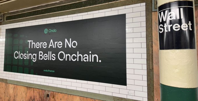 An advertisement in a subway station displays "There Are No Closing Bells Onchain" alongside the Ondo logo and ondo.finance URL, positioned next to a green and white "Wall Street" subway tile pillar. The image visually reinforces the post's message that Ondo's onchain stocks trade continuously without traditional market hours.