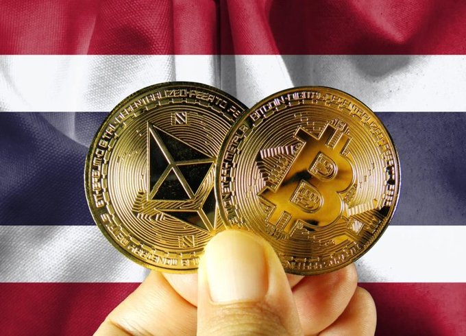 A hand holds physical representations of Bitcoin (BTC) and Ethereum (ETH) coins against the backdrop of the Thai flag, symbolizing Thailand's recent approval of BTC and ETH ETFs to begin live trading on October 16.