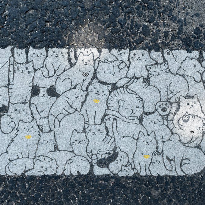 A street mural or pavement artwork depicting a group of white cats with simple facial features, including yellow dot eyes on some, resting together on asphalt.