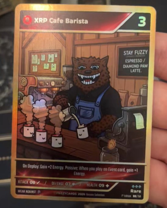 The image shows a hand holding a rare "XRP Cafe Barista" collectible card (#08/50) featuring a furry feline character making coffee, with text promoting "STAY FUZZY ESPRESSO / DIAMOND PAW LATTE" and gameplay stats including +2 Energy on deploy and +1 Energy per Event card played. The card ties into the $FUZZY token and XRP Cafe branding mentioned in the post, showcasing a character that represents the XRPL ecosystem.