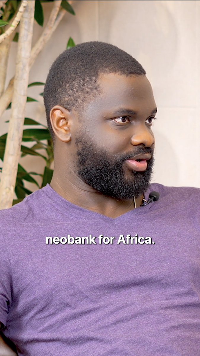 The image features a man wearing a purple shirt sitting next to a plant. The background of the photo shows a white wall, which contrasts with the man's dark hair color. There are also some text elements in the image that read "African businesses need payment rails that move at internet speed." This suggests that the man might be discussing or promoting African businesses and their needs for efficient payment systems to keep up with the fast-paced digital world.