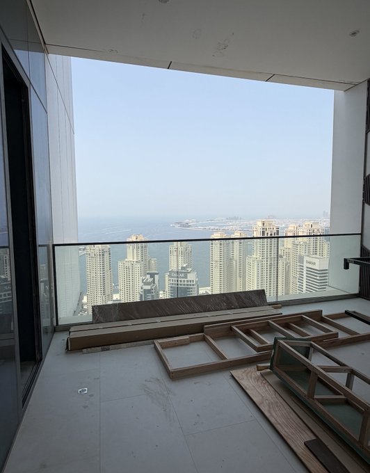 A high-rise balcony under construction overlooks Dubai's Marina skyline and coastline, with EMAAR signage visible on a building in the distance, visually representing the $3.5M Dubai penthouse purchased using Ethereum profits.