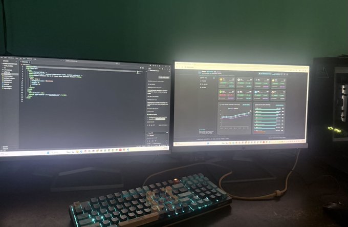 The image shows a computer setup with two monitors, one displaying a webpage and another showing a keyboard. The keyboards are positioned side by side, indicating that they might be used for different tasks or purposes. The screens display various data, possibly related to programming or other digital activities. The background of the image is green, which could be an indicator of the room's decor or lighting conditions in the area where the setup takes place.