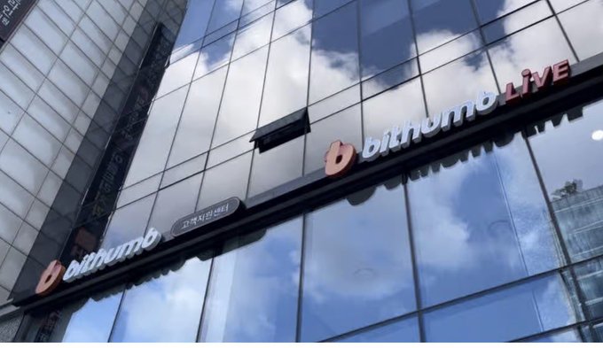 A low-angle photograph of a modern glass-fronted building displaying the 'bithumb LIVE' logo, with reflections of clouds and blue sky visible in the facade panels.