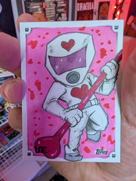 A hand holds a trading card featuring a cartoon character in a hazmat suit with a heart and blood splatter motif, signed by the artist 'TOPPS'.