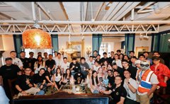 A group photo of a large team gathered around a conference table in a modern office space, appearing to celebrate or mark an occasion together.