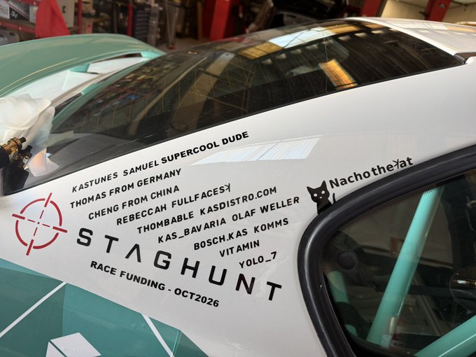 The side window of a white race car displays sponsor/donor names like 'KASTUNES,' 'SAMUEL SUPERCOOL DUDE,' 'THOMAS FROM GERMANY,' and 'CHENG FROM CHINA,' along with the text 'STAGHUNT RACE FUNDING - OCT2026' and a logo for 'NachotheCat.'