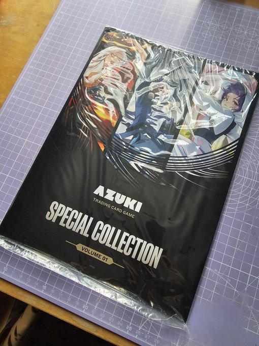 A sealed pack of the 'AZUKI SPECIAL COLLECTION VOLUME 01' trading card game featuring anime-style artwork, resting on a purple cutting mat.
