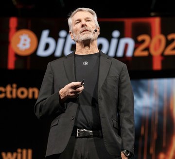 Michael Saylor, the founder of MicroStrategy (now Strategy), speaks at a "Bitcoin 2021" conference, holding a presentation clicker. The image relates to the post as it features Saylor, whose company $MSTR has just boosted its reserves to $2.55 billion to cover $STRC dividends and maintain its Bitcoin holdings.