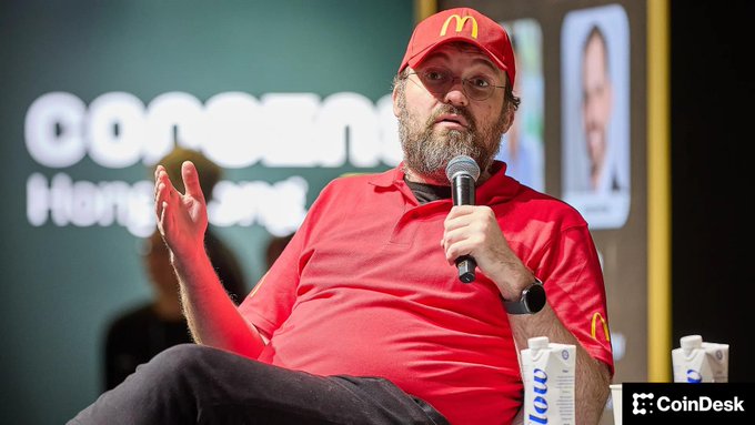 A bearded man wearing glasses and a red McDonald's cap and polo shirt speaks into a microphone at a CoinDesk 'Consensus Hong Kong' event.
