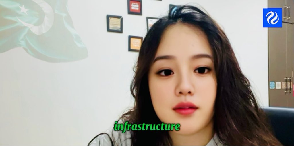 A woman with long dark hair speaks to the camera in a video, with a Turkish flag, framed certificates on the wall, and the green subtitle 'infrastructure' displayed below her.