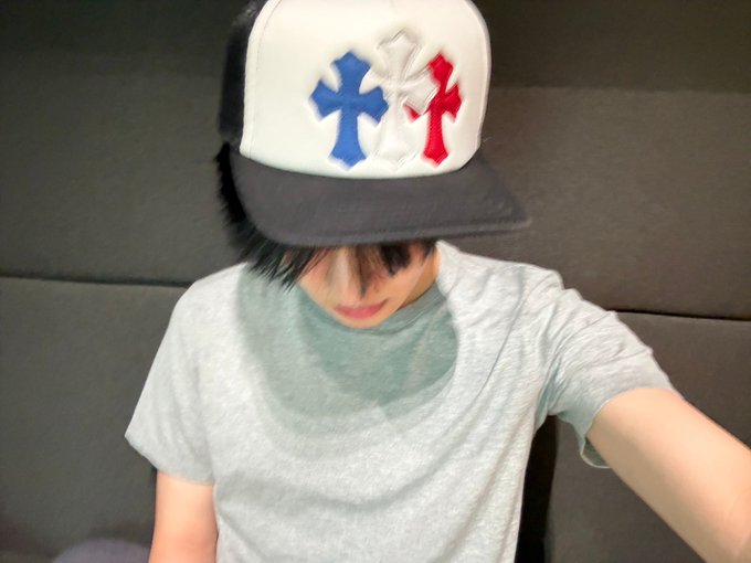 A person wearing a gray t-shirt and a white and black snapback cap with red, white, and blue cross designs tilts their head down, hiding most of their face beneath the brim. The post's tag "#LEO #리오" suggests this is a fan photo or practice update related to the artist Leo, with the cap's bold design fitting his style.
