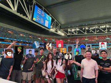 A group of people pose for a photo at a stadium, many wearing "OKX" branded shirts and jerseys, with a large scoreboard visible in the background. The image accompanies the post about attending an OKX-sponsored event to watch a game, highlighting how the experience revealed the brand's extensive presence throughout the city.