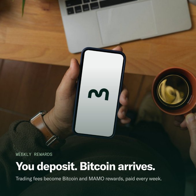 A person holds a phone displaying the MAMO logo while sipping coffee beside a laptop, with overlay text reading "WEEKLY REWARDS — You deposit. Bitcoin arrives. Trading fees become Bitcoin and MAMO rewards, paid every week." The image visually reinforces the post's message of earning Bitcoin rewards through MAMO deposits, showing the app in a casual everyday setting.