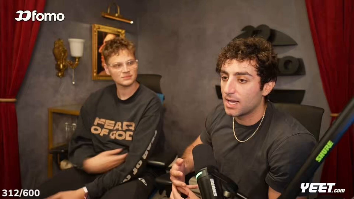 The image shows two men sitting close together, appearing to talk or having a discussion in front of a camera. They are positioned within a room with curtains behind them. One man is wearing glasses and sits beside another person who has long curly hair. Both individuals seem focused on their conversation, which appears to be centered around the trading of goods for money or virtual currency on GIGA, as indicated by a post on the platform Solana.