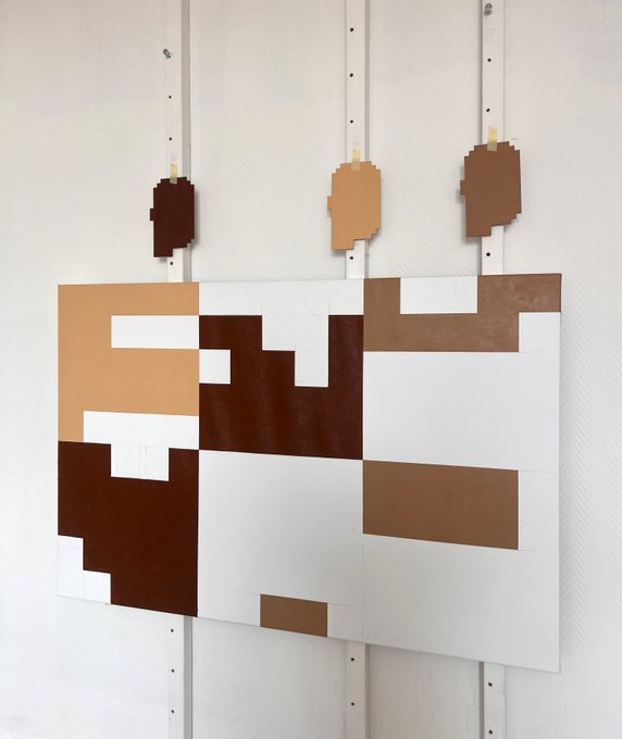 A pixel art painting mounted on a white wall, depicting abstract brown and tan pixelated shapes resembling faces or figures.