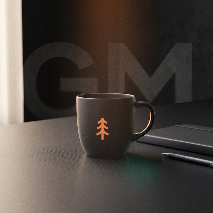 A black ceramic mug with a glowing orange tree symbol sitting on a dark desk next to a stylus pen, with a large "GM" logo faintly visible in the background.