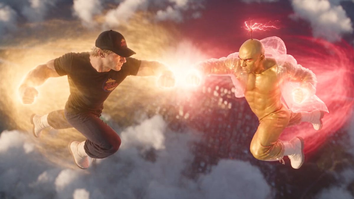 A dynamic image of two figures flying through the clouds, one in a black cap and shirt surrounded by golden energy, the other a gold-skinned figure with a lightning-bolt antenna surrounded by red energy.
