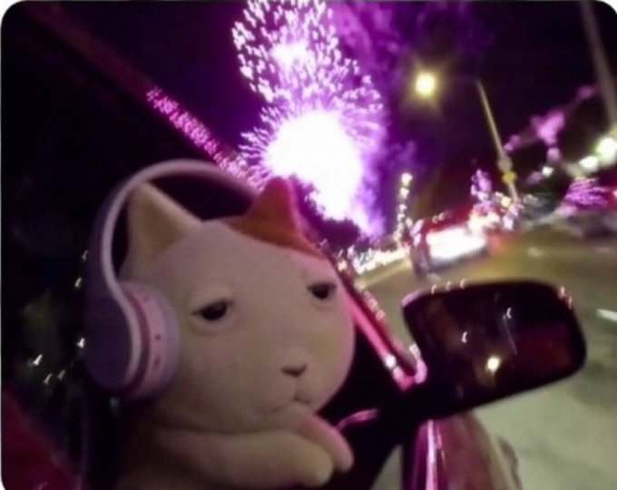 A white cat figurine wearing pink headphones sits in a car at night with fireworks bursting in the background, capturing a chill, celebratory vibe that fits the "good morning crypto enthusiasts" mood of starting the day with energy and optimism.