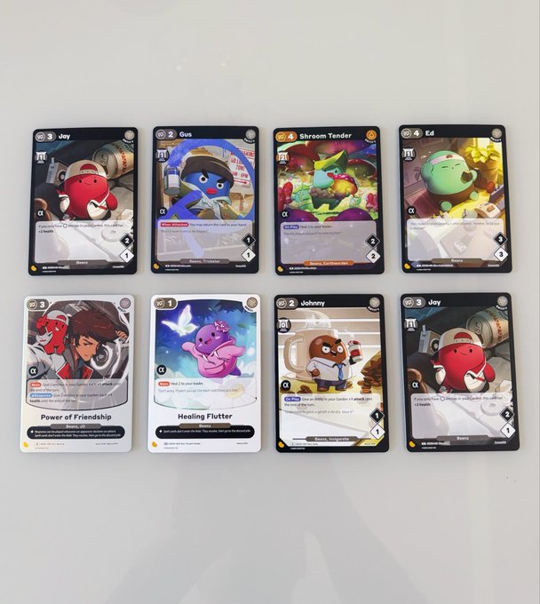 Eight Disney Lorcana trading cards arranged in two rows on a white surface, including characters like Joy, Gus, Shroom Tender, Ed, Power of Friendship, Healing Flutter, and Johnny.