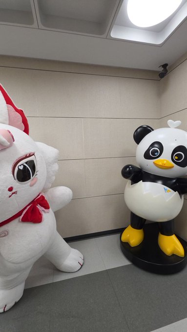 Two mascot statues - a white cat character with a red bow and a black and white penguin - standing against a tiled wall.