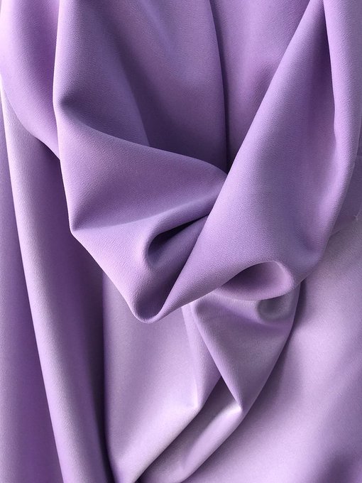 Close-up photograph of lavender-purple satin or silk fabric with soft folds and a smooth, shiny texture.