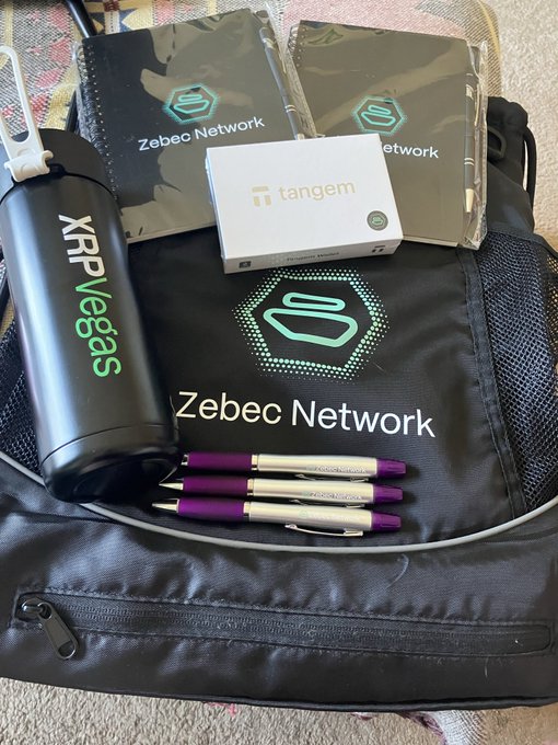 A collection of Zebec Network (ZBCN) branded merchandise including a black backpack, water bottle labeled "XRP Vegas," a Tangem crypto wallet, notebooks, and promotional pens, gifted by @CaptainZackZBCN as a gesture of appreciation within the crypto community.