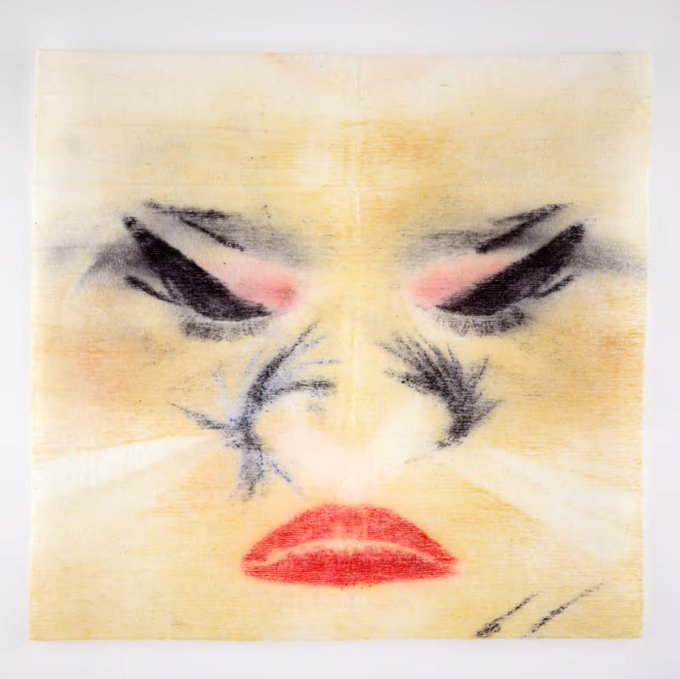 An artistic drawing or painting of a face with heavy black and pink eye makeup, prominent eyelashes, and red lips, created on what appears to be a folded paper napkin.