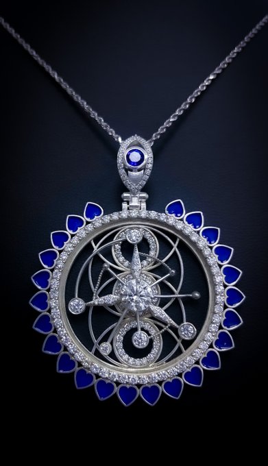 A silver-toned pendant necklace featuring an intricate geometric star design in the center, surrounded by blue heart-shaped and small clear gemstones.