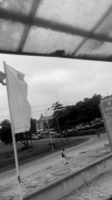 A black-and-white photo taken under a canopy, showing a flag with 'GTCO' branding, a street scene with a person walking, and a sign for GTCO Guaranty Trust.