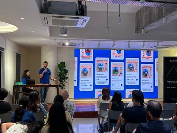 A presenter addresses a crowd during a tech event, showcasing a slide deck featuring colorful AI-generated illustrations of various "Genie" characters, which complements the post about demonstrating their in-house AI agent and Minds platform with thanks to sponsors Lorong AI, Notion, and Vercel.