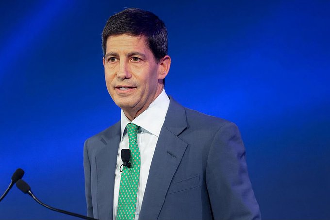 A man in a blue suit and green tie stands at a podium with microphones against a blue backdrop, appearing to deliver remarks. The image relates to the post about the Federal Reserve raising interest rates by 25 basis points, suggesting he may be a Fed official announcing or commenting on the rate decision.