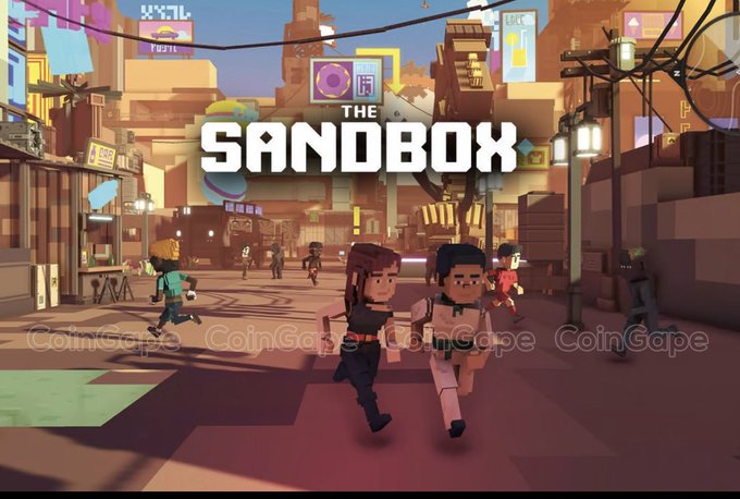 A promotional image for "THE SANDBOX" video game, showing blocky voxel characters running through a vibrant pixel-art cityscape, watermarked with "CoinGape".