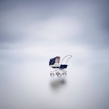 A small, vintage-style baby carriage floats alone against a vast, minimalist gradient background, its tiny scale emphasizing an almost dreamlike emptiness. The serene composition fits the post's "gm / The Shot / The Spot" theme, presenting a quiet, stylized moment rather than any legible text or numbers.